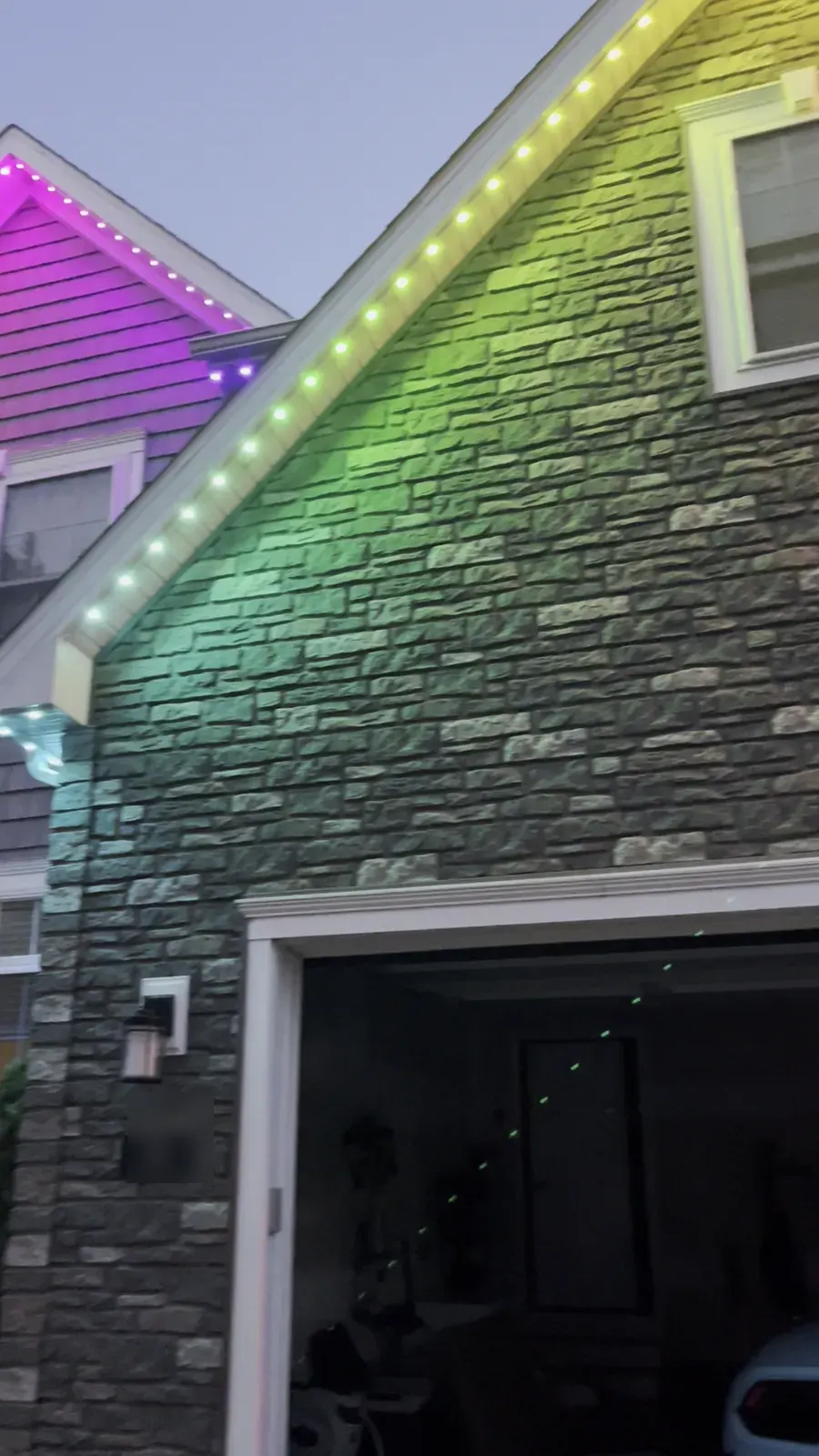 Stone gable and garage lit in a rainbow of colors by permanent puck lights at dusk